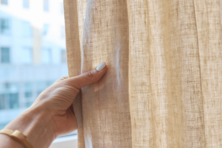 thick beige curtains held hung up and held by homeowner 