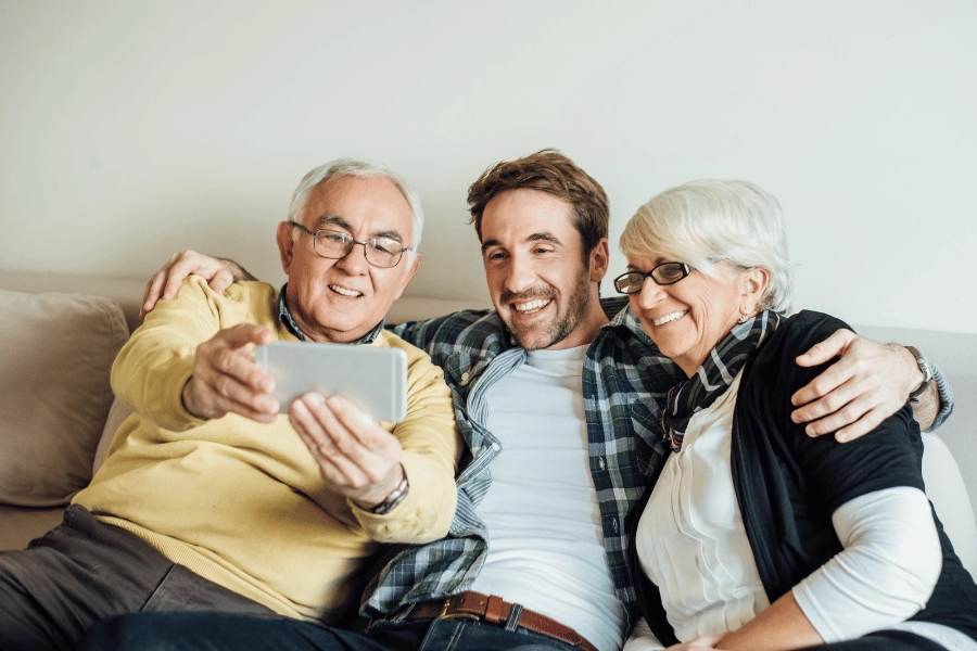 young adult taking a picture with older parents while sitting on the couch