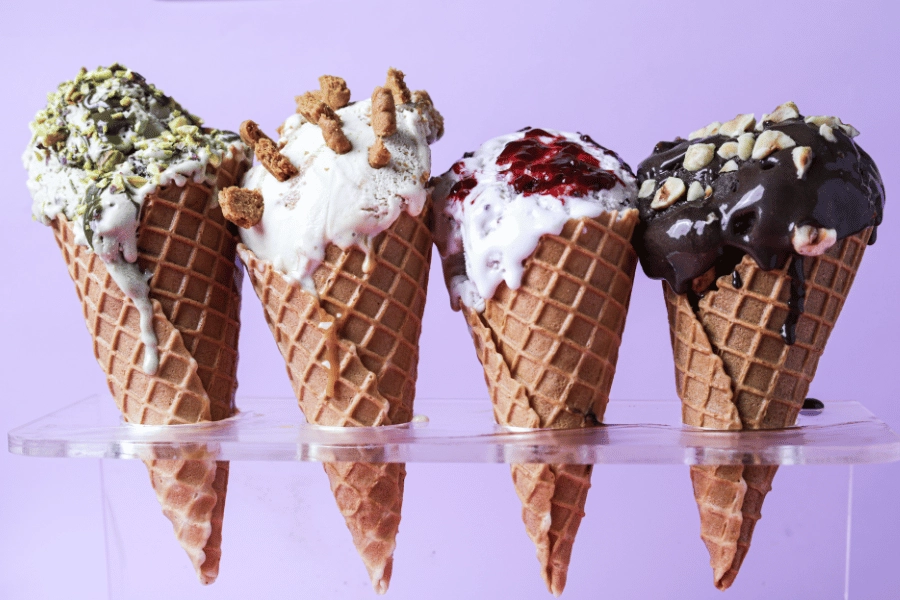 four ice cream cones lined up with different flavors of ice cream and various toppings
