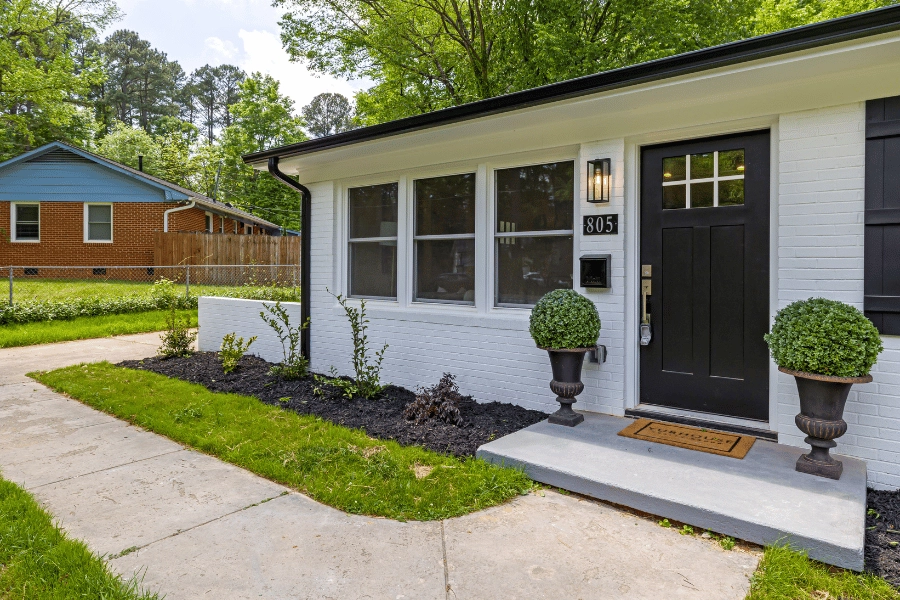 cute family home with white brick and black front door and sidewalk