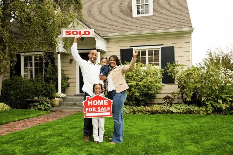 family of four holding a sold sign in front of a single-family home