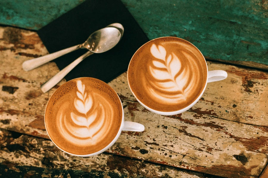 cute latte art in two mugs of coffee on a table with spoons on a napkin