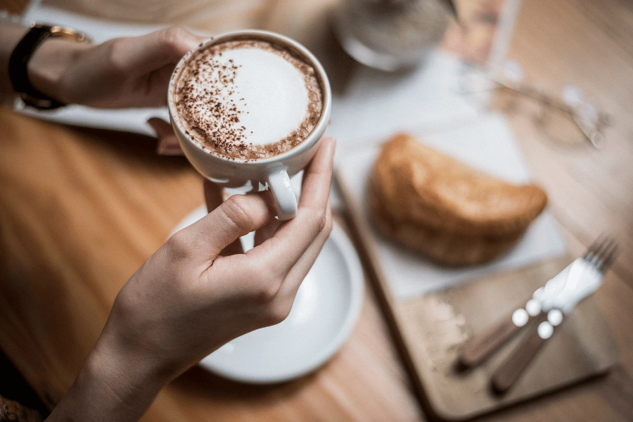 hot latte in a white mug and pastry on a table 