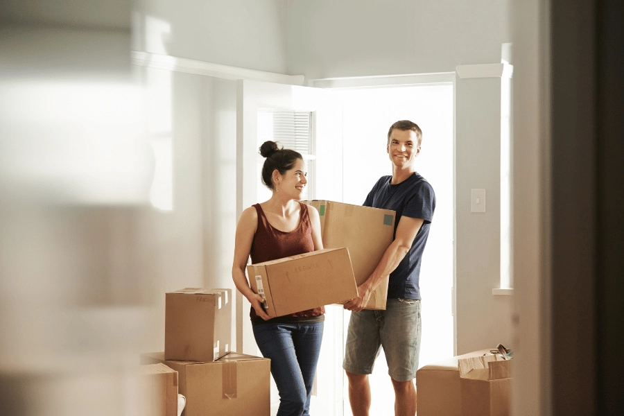 couple holding moving boxes and walking into their first home