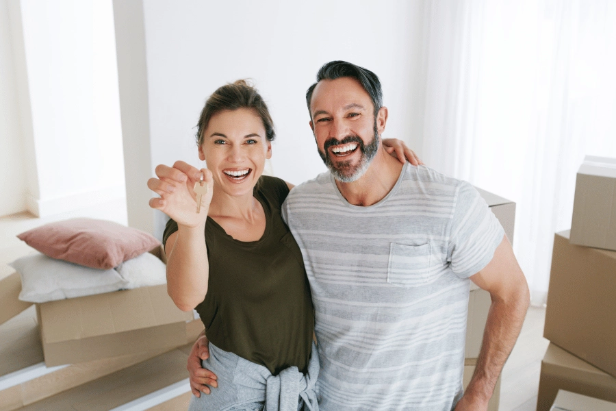 happy first time home buyer couple holding house keys surrounded by moving boxes