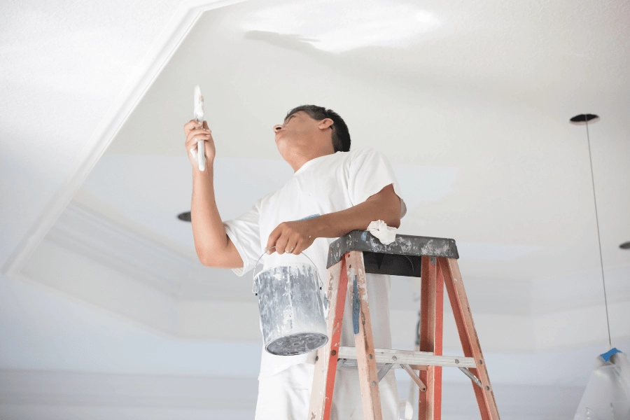painter standing on a ladder painting ceiling after popcorn ceiling removal