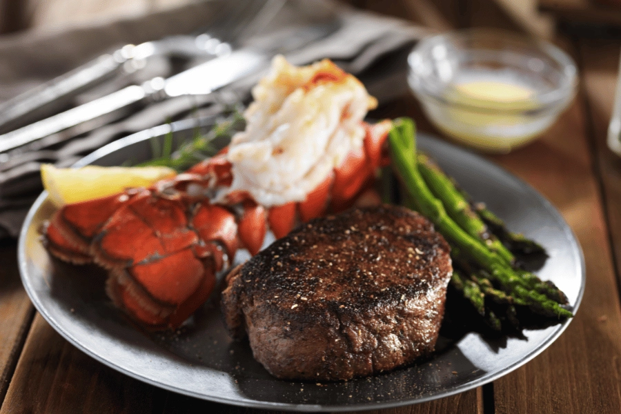 steak and lobster and asparagus on a silver plate at a restaurant