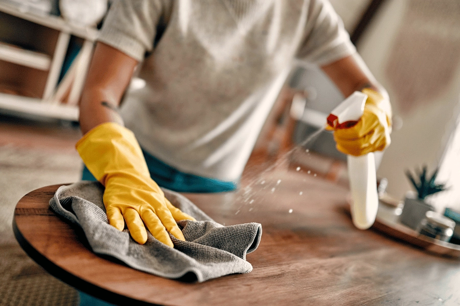 homeowner dusting and cleaning table with yellow gloves and cleaning solution