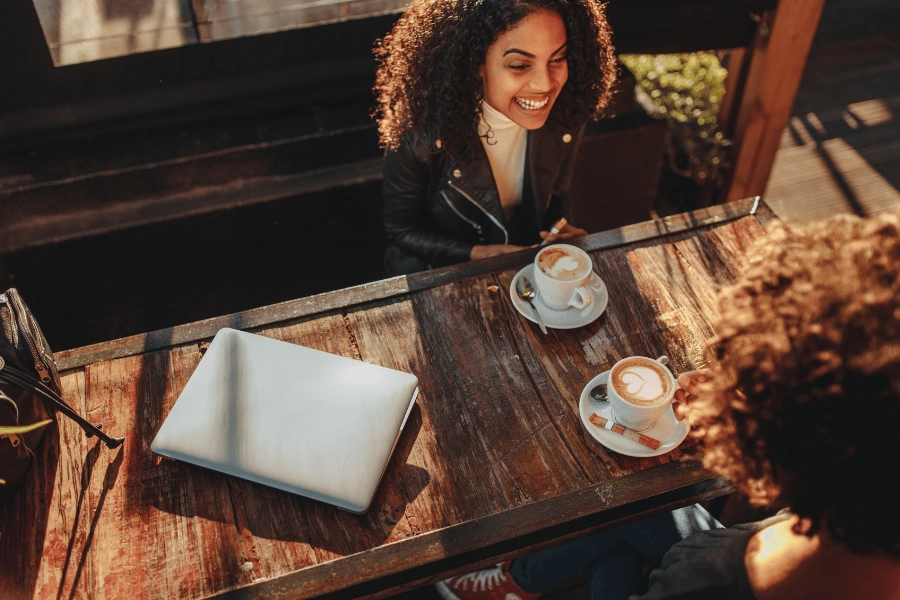 two friends sitting outside at a coffee shop talking with lattes