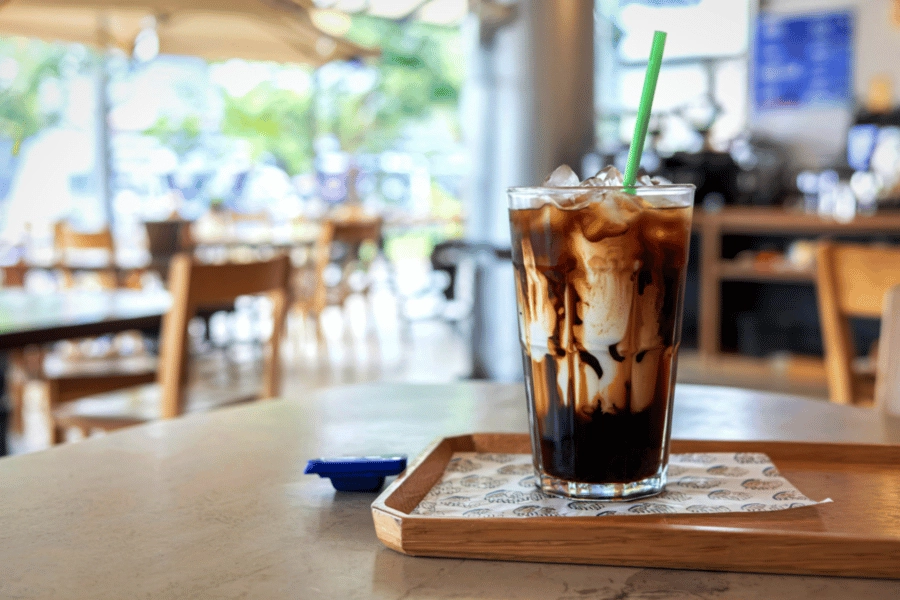glass of iced coffee on a table in a coffee shop with a green straw