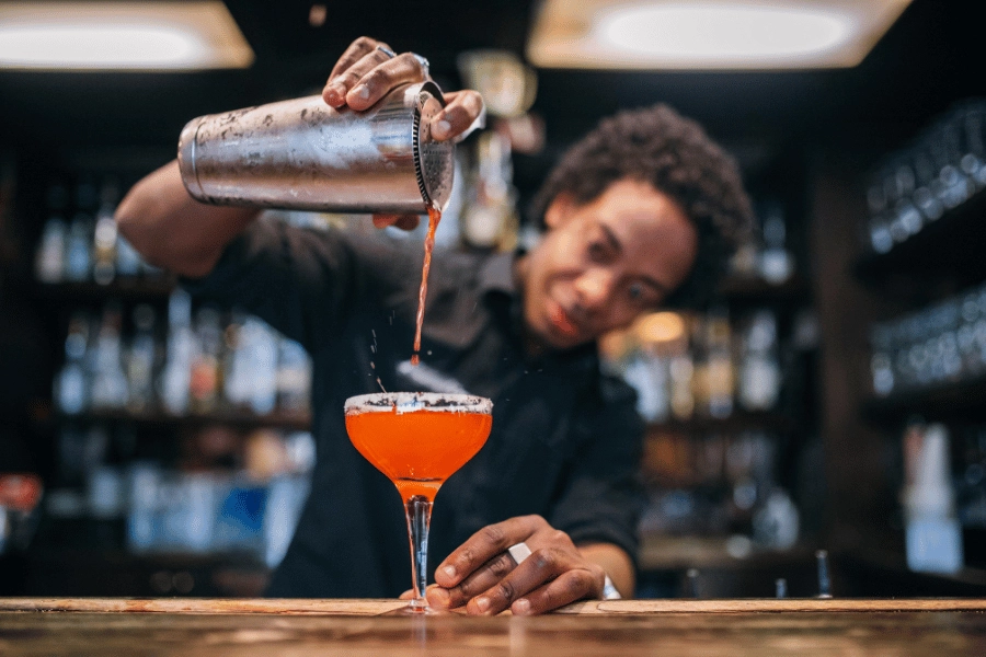 bartender making a drink and pouring it into a glass at a bar