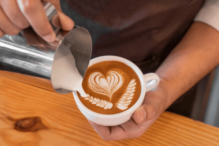 barista making cute heart latte art in a white coffee mug