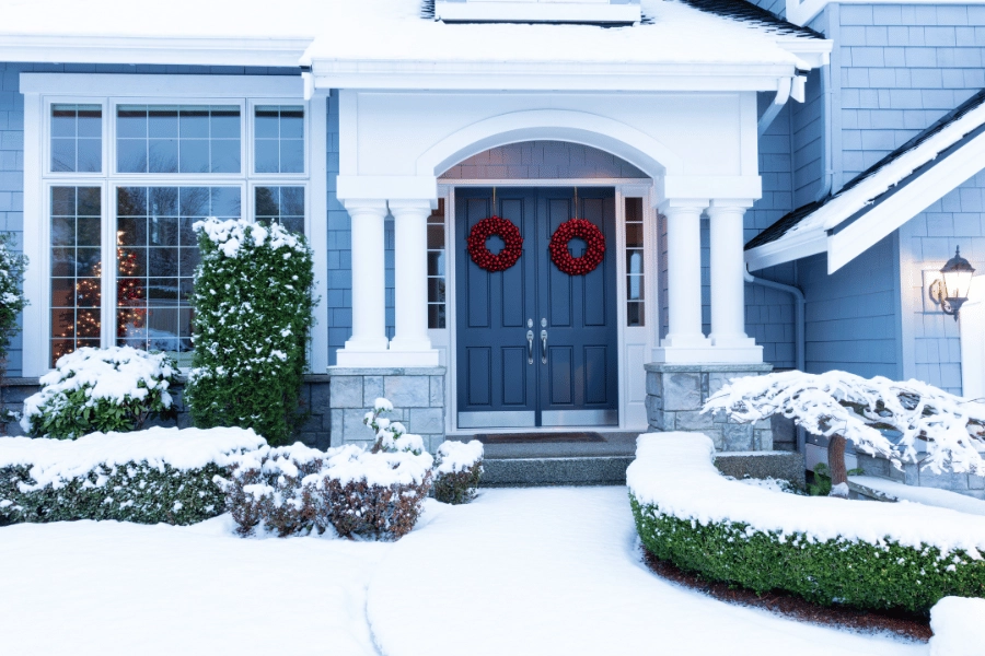 snowy home with christmas decorations and wreaths on the front doors