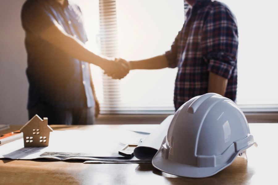 home seller shaking hands with builder after a sale and construction hat sitting on the table